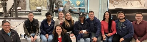 group of eleven people sitting on a bench in peabody museum